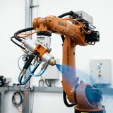 ロボットアームの先端スプレーノズルから塗料が霧状に噴射されている塗装自動化システムの実写写真